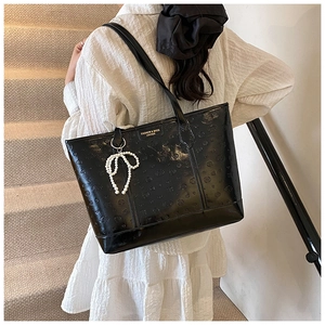 Detail of black embossed patent leather tote bag with elegant pearl bow accessory