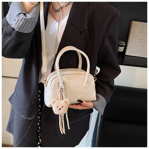 Détail d'un sac Boston crème avec pendentif ours et bandoulière sur un costume gris