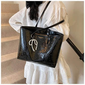 Detail of black embossed tote bag with glossy finish and pearl bow charm accessory