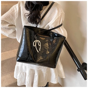 Close-up of black tote bag with embossed cartoon textures and pearl bow charm detail