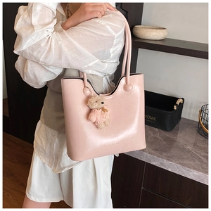 Detail view of pink leather tote bag featuring a cute knit sweater bear pendant charm