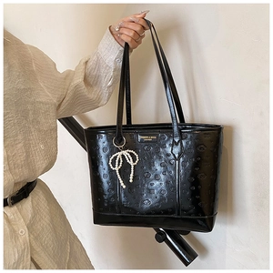 Detail of black floral embossed tote bag featuring a pearl bow charm and long handles