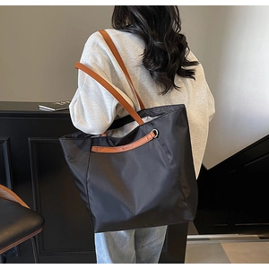 Side view of large black oxford tote bag with brown leather straps on a model