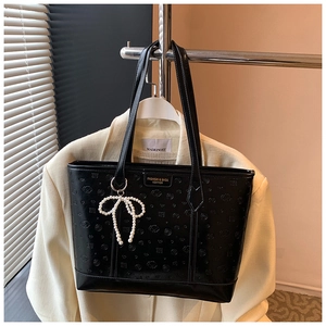 Detail of embossed black leather tote bag with pearl bow charm and dual straps