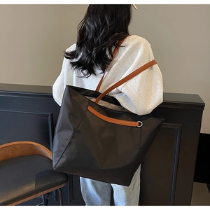 Side view of a large black nylon tote bag with brown straps and silver metal ring detail