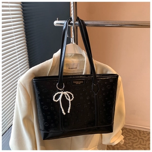Detail of black embossed leather tote bag featuring a pearl bow pendant and art patterns