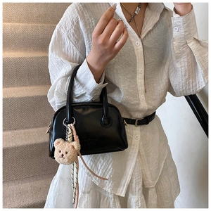 Détail du sac Boston noir mat avec breloque ours sur une robe blanche élégante