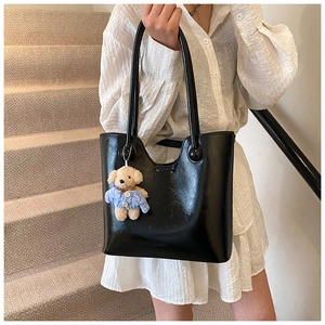 Detail of black shiny bucket bag with a cute teddy bear charm on minimalist background