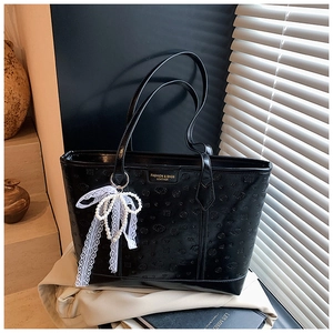 Detail of large black embossed tote bag with lace pearl bow charm and twin handles
