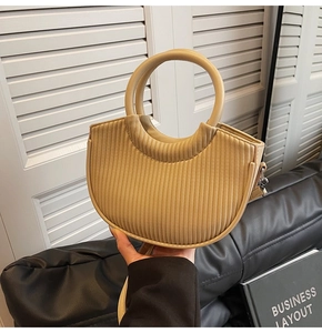 Detail of minimalist beige bucket bag with vertical pleated texture and round ring handle