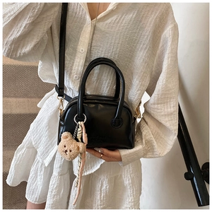 Détail d'un sac à main noir brillant en simili cuir avec un charmant pendentif ours