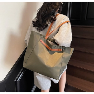 Detail of olive green nylon tote bag featuring brown leather straps and embossed logo