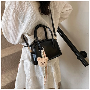 Détail du sac à main noir en similicuir brillant avec charm ours en peluche et cordon