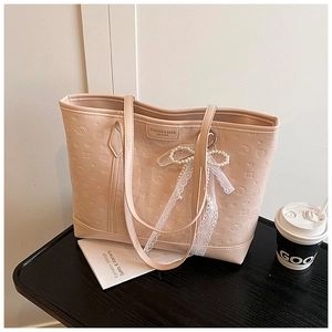 Detail of beige tote bag featuring cartoon embossed texture and pearl lace bow charm