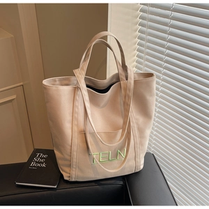Close-up of beige canvas tote bag featuring green TELN embroidery and side pocket