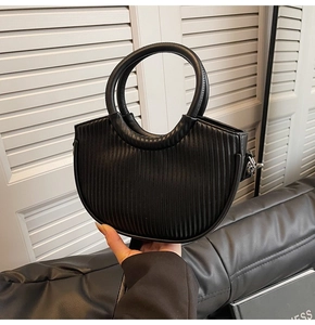 Detail of black pleated crescent handbag featuring round rigid handle and matte leather finish