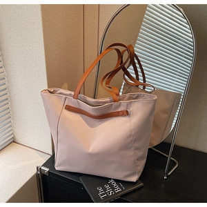 Detail of light pink nylon tote bag featuring brown leather straps and metallic accents