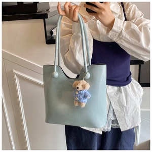 Detail of light blue leather tote bag featuring a cute beige teddy bear plush pendant