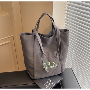 Deep gray canvas tote bag with TELN embroidery on a leather bench in natural light