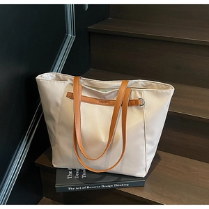 Close-up of beige Oxford fabric tote bag with brown leather handles on wooden stairs