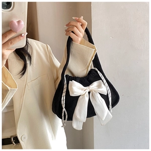 Close-up of black corduroy handbag with white satin bow detail and drawstring closure