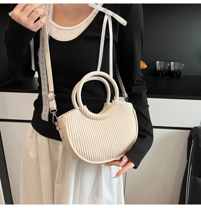 Close-up of beige half-moon bucket bag featuring vertical pleated texture and ring handle