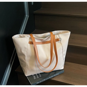 Close-up of cream nylon tote bag with brown faux leather trim on wooden stairs