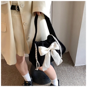Detail of black corduroy handbag featuring a large white satin bow and drawstring closure