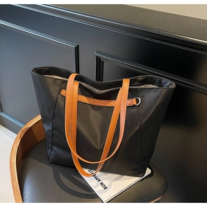 Close-up of black nylon tote bag with brown leather straps and metal D-ring detail