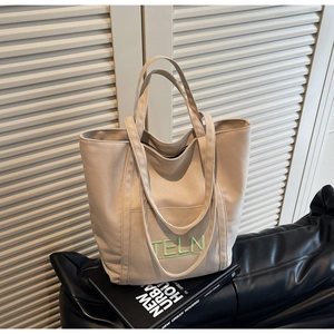 Detail of beige canvas tote bag featuring green TELN letter embroidery and dual straps