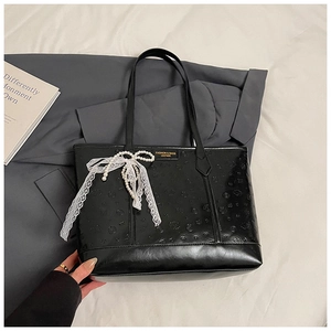 Detail of black faux leather tote with heart embossing, lace bow, and pearl charm