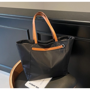 Detail of black nylon tote bag featuring brown leather handles and silver metal ring accent