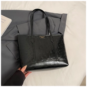 Detail of black leather tote bag featuring embossed patterns on white bedding background