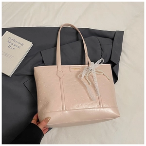 Detail of pink embossed tote bag featuring gold logo plate and lace pearl charm accessory