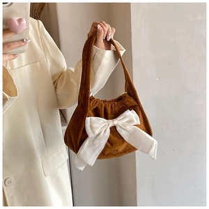 Brown corduroy handbag with a large white satin bow detail shown in a lifestyle setting
