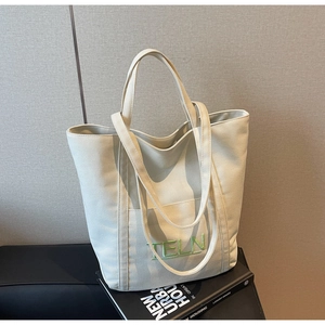 Detail of off-white canvas tote bag featuring green TELN embroidery on a black magazine