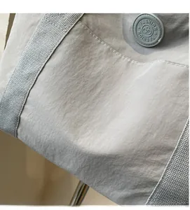 Détail de la texture en nylon souple et écusson rond sur le sac fourre-tout gris clair
