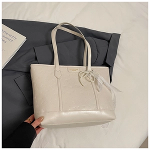 Detail of a beige tote bag featuring floral embossed patterns and a pearl bow charm