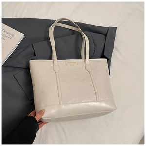 Close-up of beige tote bag featuring embossed pattern and gold metal logo plaque