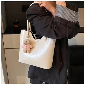 Close-up of white glossy faux leather tote bag with wavy rim and cute teddy bear charm