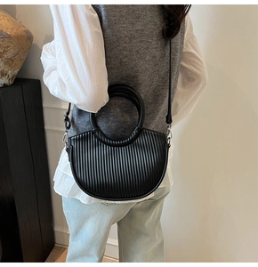 Detail of black pleated crescent bucket bag with round handle and detachable shoulder strap