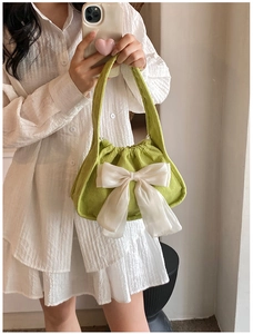 Close-up of green corduroy handbag featuring a large white satin bow and drawstring top