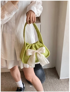Detail of green corduroy handbag with a large creamy white satin bow decoration