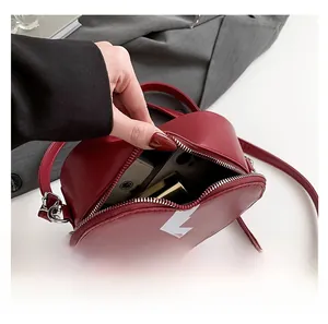 Detail view of heart-shaped crossbody bag capacity showing phone and lipstick storage