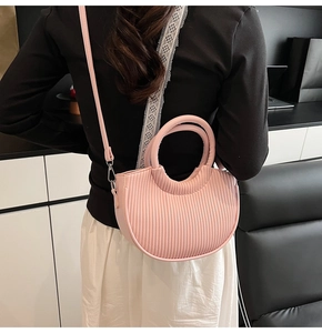 Pink pleated crescent bucket bag with circular handles and leather strap on model