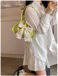 Detail of trendy light green corduroy handbag featuring a large white satin bow accent