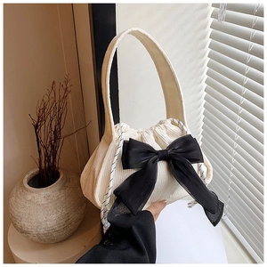 Detail of white corduroy handbag featuring a large black chiffon bow and drawstring closure