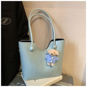 Close-up of light blue leather bucket bag with sphere handle and cute bear charm