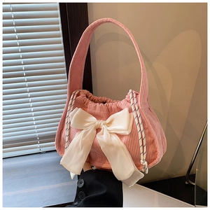 Sac à main en velours côtelé rose avec grand nœud blanc et cordon tressé sous lumière douce