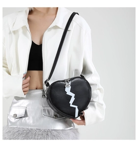 Detail of a heart-shaped black crossbody bag with white zigzag pattern on a model